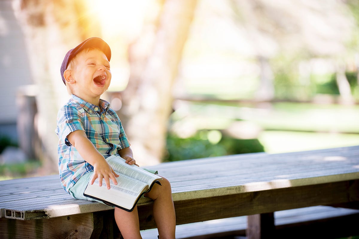 A boy laughing on a bench with a book