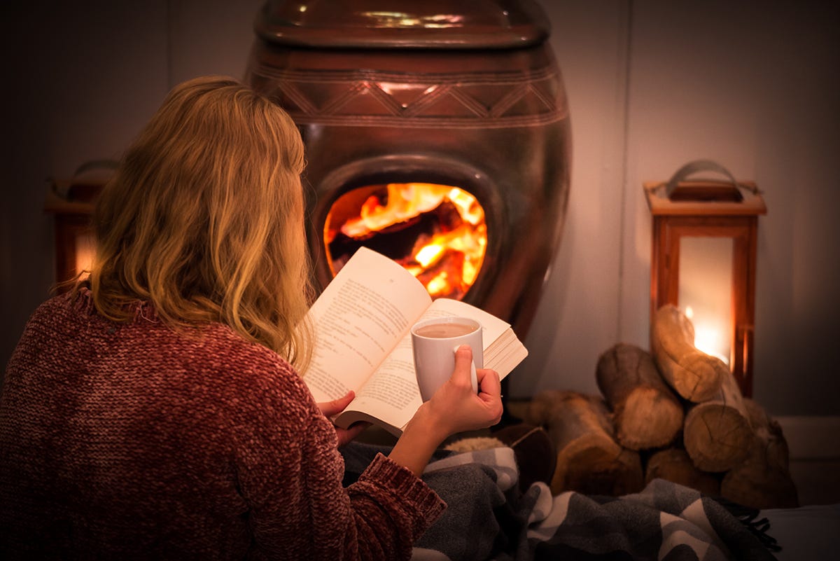 Woman sat in front of a fire with a book and hot drink